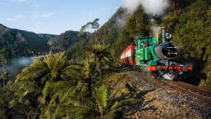 a green train traveling down the tracks in the mountains at West Coaster Motel in Queenstown
