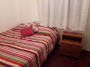 1 cama con almohada roja y mesa de madera en Casa de Andrea en Esquel