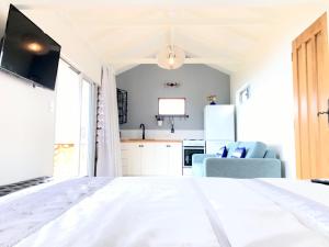 a bedroom with a white bed and a kitchen at Piha Tiny House in Piha