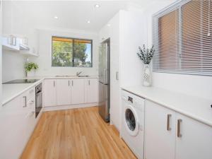 a kitchen with white cabinets and a washer and dryer at Waves Appartment in Kiama
