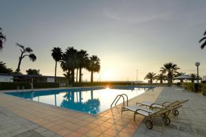 une piscine avec des bancs et des palmiers et le coucher du soleil dans l'établissement Parador de Benicarló, à Benicarló
