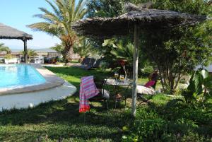 a woman sitting under an umbrella next to a pool at Casa Entre Armonías in Zahara de los Atunes