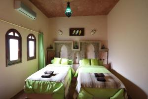 a bedroom with two beds with green sheets and windows at Riad Moha in Merzouga