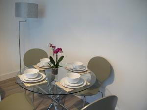 uma mesa de vidro com pratos e copos e um vaso com flores em Westpark Apartment em East Kilbride