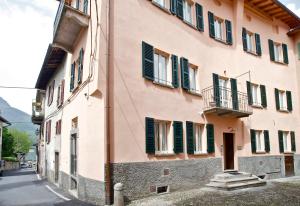 a pink building with green shutters on a street at Locanda della Maria in Bellagio