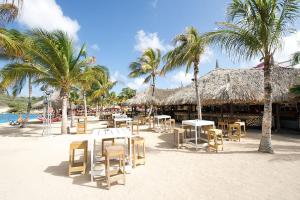 una playa con mesas, sillas y palmeras en Villa Sol Paraiso en Jan Thiel