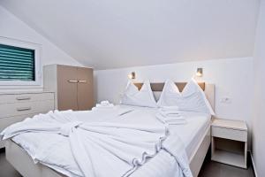 a white bedroom with a large white bed with white sheets at Apartments Bisernica-with pool in Ražanj