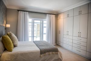 a bedroom with a bed with white cabinets and a window at The Whale on Main B&B in Hermanus
