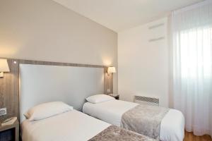 a hotel room with two beds and a window at Séjours & Affaires Reims Clairmarais in Reims