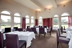 un comedor con mesas y sillas blancas y ventanas en Lancemore Mansion Hotel Werribee Park en Werribee