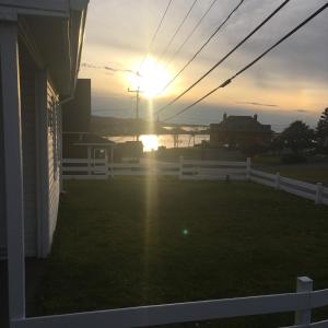 a sunset over a white fence with the sun setting at La petite maison sur la côte in Sainte-Anne-des-Monts