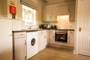 a kitchen with white cabinets and a washer and dryer at Tissington Cottage- Darwin Lake Holiday Village in Matlock