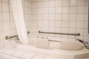 a white tub in a bathroom with white tiles at Rodeway Inn Abbotsford in Abbotsford +24 photos