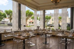 un restaurante con mesas, sillas y ventanas grandes en The Originals City, Hôtel Napoléon, La Roche-sur-Yon (Inter-Hotel) en La Roche-sur-Yon