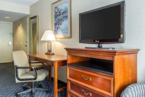 a hotel room with a television on a dresser with a desk at Clarion Hotel and Conference Center in Ronkonkoma