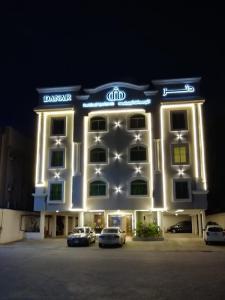 Danar Hotel Apartments 5 في الخبر: مبنى مضاء فيه سيارات متوقفة أمامه