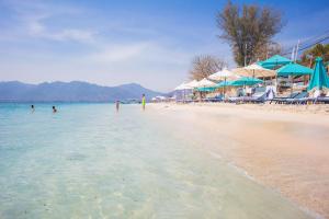 a beach with people in the water and umbrellas at Sunrise Resort in Gili Air