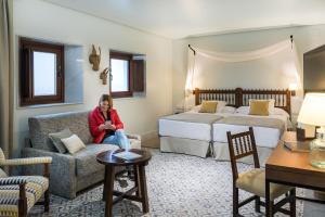 una mujer sentada en una habitación de hotel con dos camas en Parador de Arcos de la Frontera en Arcos de la Frontera