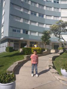 un niño pequeño parado en una acera frente a un edificio en el cabo frente al mar en Mar del Plata