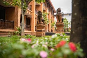 a building with statues in front of a yard with flowers at Phor Liang Meun Terracotta Arts - SHA Extra Plus in Chiang Mai