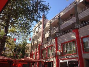 a building with red windows and a tree and umbrellas at Yalçın Otel in Antalya