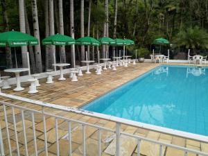 a pool with green umbrellas and tables and chairs at Pousada Scursel in Ibirama