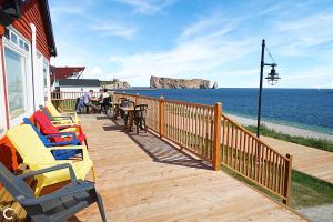 a wooden deck with chairs and tables and the ocean at Hotel-Motel Fleur de Lys in Perce