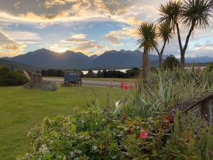 a garden with a truck on a road with mountains at Manapouri Lakeview Motor Inn in Manapouri