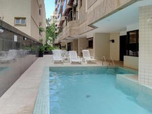 a swimming pool with white chairs and a building at Ocean Flat in Rio de Janeiro