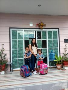 a woman and two children standing on a porch with luggage at Patchy & PPraw Family in Ubon Ratchathani