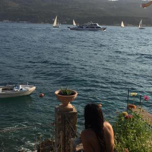 a woman sitting on a railing looking at boats in the water at Roditses Beach Sea Front Apartments in Samos