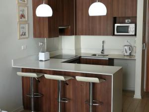 una cocina con armarios de madera y una barra con taburetes en Excelente departamento en Las Condes en Santiago