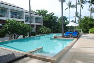 a swimming pool with two blue chairs and a building at The Park Samui in Choeng Mon Beach