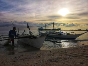 a man standing next to a boat on the beach at Stevrena Accommodations in Bantayan Island