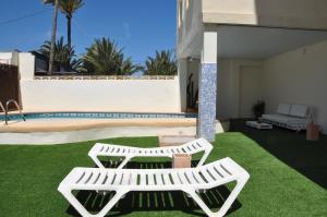 two white benches sitting on a lawn next to a pool at Apartamentos Acuario in Denia
