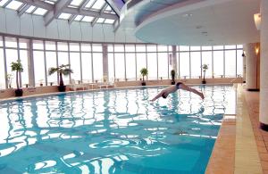 a person diving into a swimming pool in a building at Novotel Atlantis Shanghai - Breakfast in the clouds with river view in the revolving restaurant in Shanghai