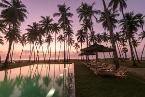 a pool with chairs and palm trees and a sunset at Kottukal Beach House by Jetwing in Arugam Bay