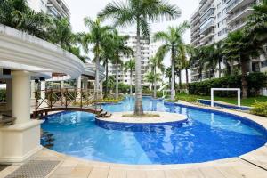 a large blue swimming pool with a bridge and palm trees at Barra Family Resort - 3 Quartos in Rio de Janeiro