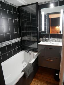 Baño de azulejos negros con bañera y lavamanos en Appartement 4 personnes au pied des pistes du Linga à CHÂTEL en Châtel