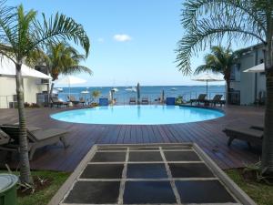 a swimming pool with palm trees and benches and the ocean at Troux aux Biches Le Cerisier A2 Mauritius in Trou aux Biches