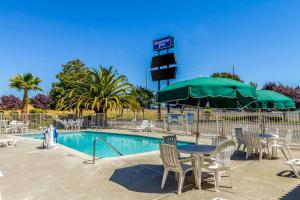 a pool with chairs and a table and a green umbrella at Rodeway Inn - Rohnert Park in Rohnert Park