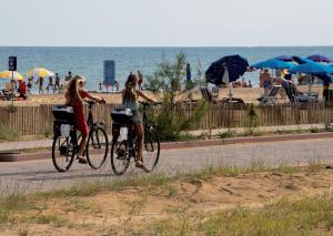 dos chicas montando bicicletas en una acera cerca de la playa en Hotel San Michele, en Bibione