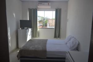 1 dormitorio con 1 cama y ventana con TV en Suítes Centro, en Arraial do Cabo