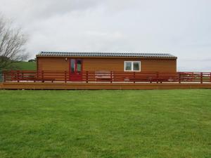 eine große Holzhütte mit einem grünen Feld davor in der Unterkunft Golden Oak Chalet in Dunbar