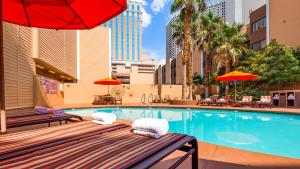 a swimming pool with two benches and a red umbrella at Best Western Plus Casino Royale - Center Strip in Las Vegas