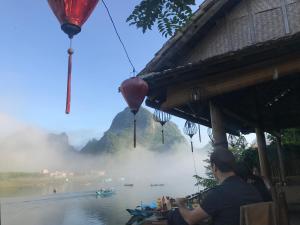 Ein Mann, der neben einem Gebäude neben einem Fluss sitzt. in der Unterkunft Phong Nha Coco House in Phong Nha