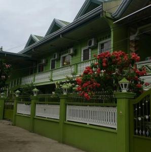 a green house with flowers on a fence at Magdalene Apartment in Balamban