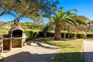 a garden with a palm tree and a stone oven at Villas Rab Palit in Rab