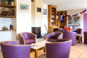 une salle d'attente avec des chaises violettes, une table et une cheminée dans l'établissement Azureva Fournols, à Fournols