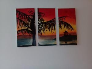 three canvases of a palm tree and a sunset at La casita de Chany in Mina Clavero